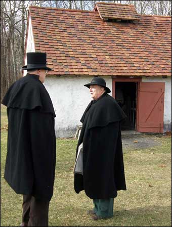 Hopewell Furnace, PA - Two colonial men talking outside of the blacksmith shop, Notice the clay tiles on the roof of the shop. When the shop caught on fire, some of the tiles needed replaced. 200 years later the same mold was found to make new tiles to replicate the old tiles
