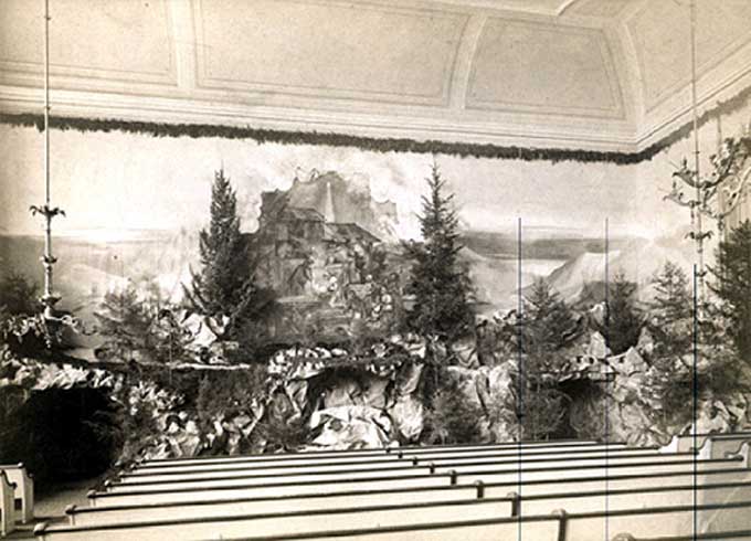 Moravian Christmas History - The 1748 display can also be considered a precursor of the Putz and the Christmas decorations of the sanctuary. An early photographic image of such decoration in Bethlehem’s Central Moravian Church dates from 1884. Work on the decorations began on December 15th; according to the diary, services had to be moved to the Old Chapel on the Fourth Sunday of Advent because of the “very elaborate decoration in progress in the church.” Attendance on Christmas Eve was extraordinarily large that year: “The elaborate and beautiful decoration attracts many persons, not members of the Congregation, to the church. The best of order prevailed however, and on the whole, all passed off nicely.” Note on the photograph how the liturgist’s table was incorporated into the display! The minister led the Christmas services from  behind this table.